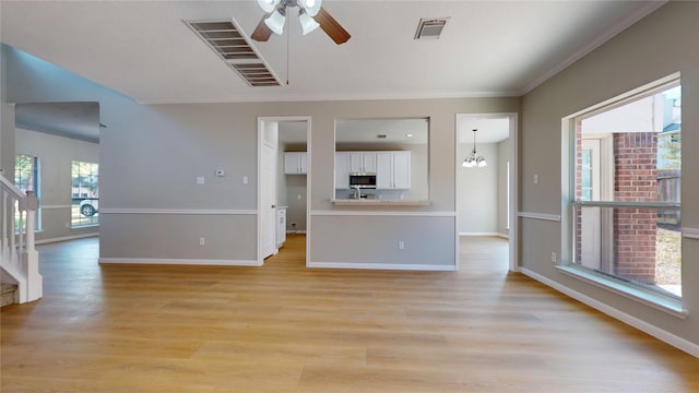 unfurnished living room with light hardwood / wood-style floors, crown molding, ceiling fan with notable chandelier, and plenty of natural light