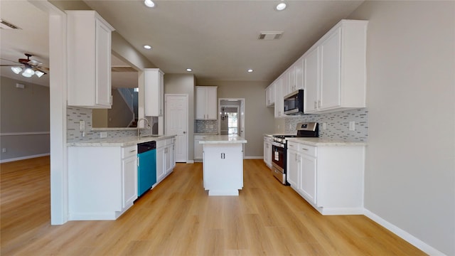 kitchen with white cabinets, appliances with stainless steel finishes, light stone countertops, light wood-type flooring, and a center island