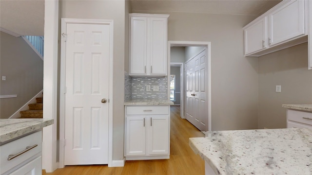 kitchen with light stone countertops, white cabinetry, light wood-type flooring, and tasteful backsplash