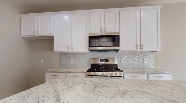 kitchen featuring appliances with stainless steel finishes, white cabinets, light stone countertops, and backsplash