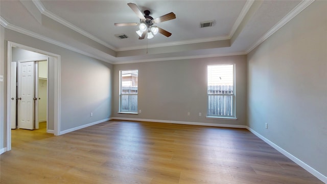 empty room with crown molding, a tray ceiling, light wood-type flooring, and ceiling fan