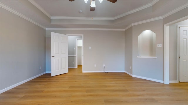 empty room with a raised ceiling, crown molding, light wood-type flooring, and ceiling fan