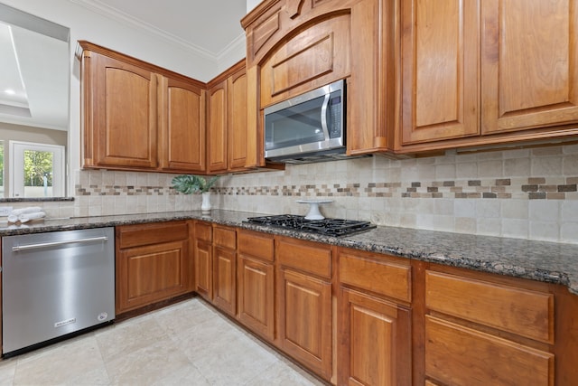 kitchen with tasteful backsplash, light tile patterned flooring, stainless steel appliances, dark stone countertops, and ornamental molding