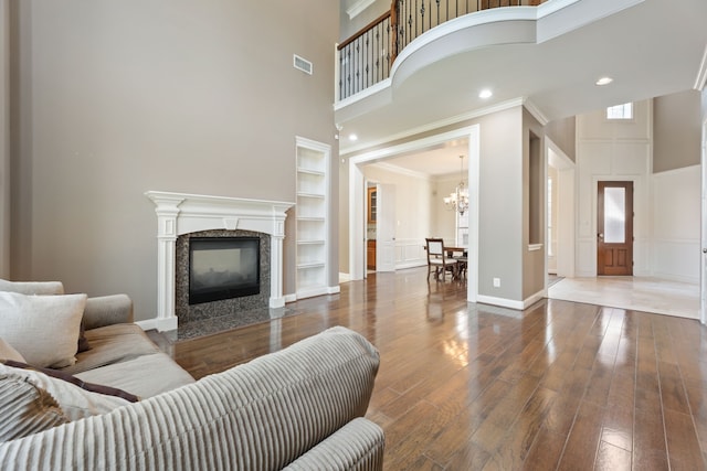 living room featuring wood-type flooring, a premium fireplace, crown molding, built in shelves, and a towering ceiling