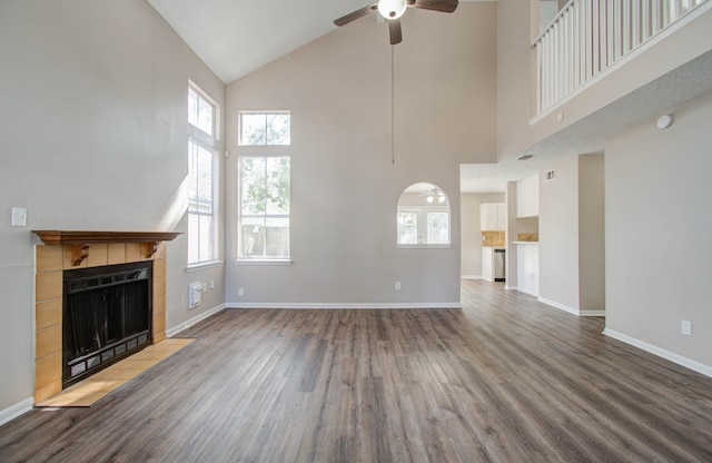 unfurnished living room featuring hardwood / wood-style floors, a tiled fireplace, high vaulted ceiling, and plenty of natural light