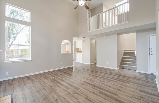 unfurnished living room with a high ceiling, wood-type flooring, and ceiling fan