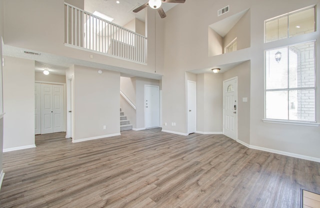 unfurnished living room featuring a towering ceiling, light hardwood / wood-style flooring, and ceiling fan