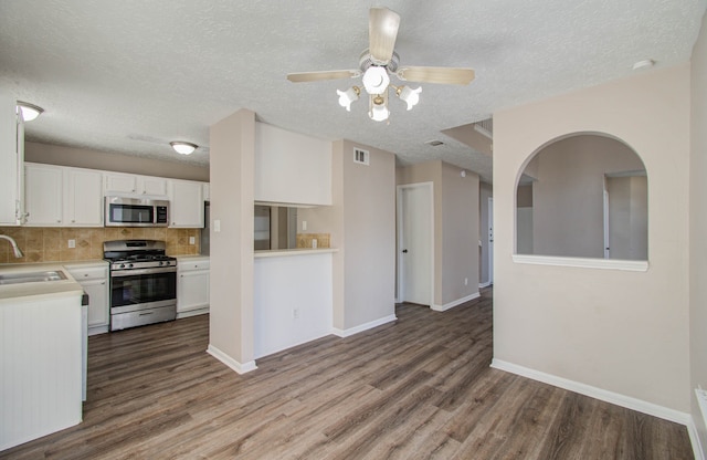 kitchen with a textured ceiling, white cabinetry, stainless steel appliances, and wood-type flooring