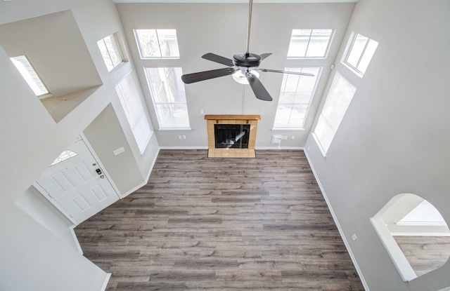 unfurnished living room featuring a high ceiling, a fireplace, hardwood / wood-style flooring, and ceiling fan