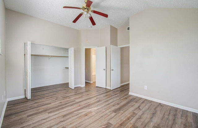 unfurnished bedroom featuring lofted ceiling, a closet, light hardwood / wood-style flooring, a textured ceiling, and ceiling fan