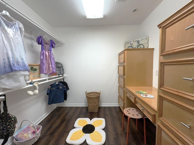 spacious closet with built in desk and dark hardwood / wood-style flooring