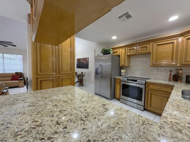 kitchen with tasteful backsplash, appliances with stainless steel finishes, light stone countertops, and light tile patterned floors