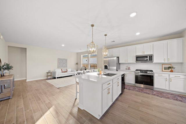 kitchen with sink, appliances with stainless steel finishes, decorative light fixtures, light hardwood / wood-style floors, and white cabinetry