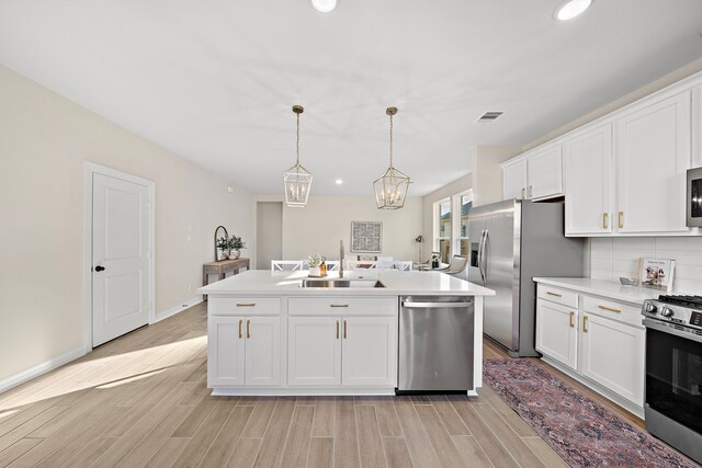 kitchen with light hardwood / wood-style floors, white cabinetry, hanging light fixtures, and appliances with stainless steel finishes