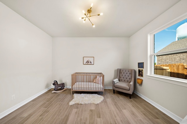 bedroom featuring a chandelier, a nursery area, and light hardwood / wood-style floors