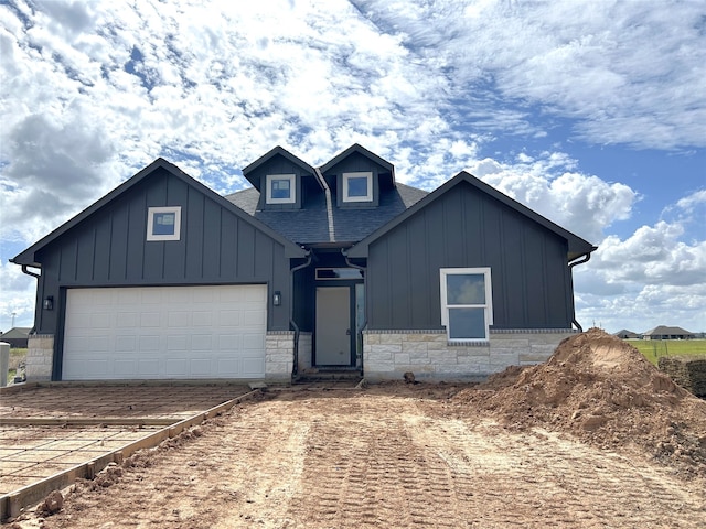 view of front of property with board and batten siding, stone siding, roof with shingles, and an attached garage