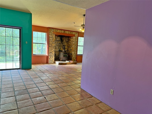 unfurnished living room with a wood stove, a textured ceiling, and ceiling fan