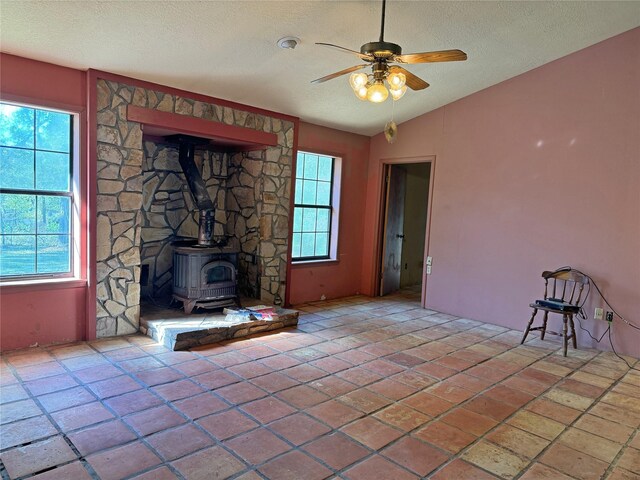 unfurnished living room featuring a wood stove, a textured ceiling, vaulted ceiling, and ceiling fan