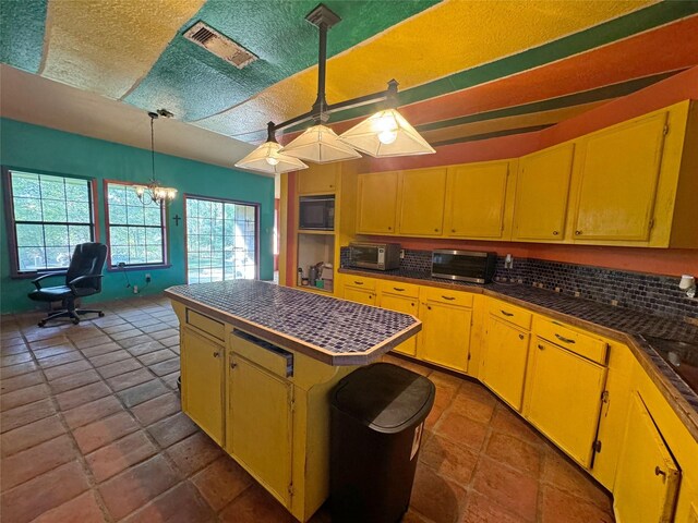 kitchen featuring dark tile patterned floors, a kitchen island, black microwave, backsplash, and pendant lighting