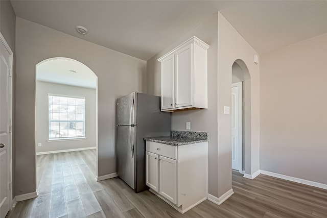 kitchen with white cabinetry, light hardwood / wood-style floors, dark stone counters, and stainless steel fridge