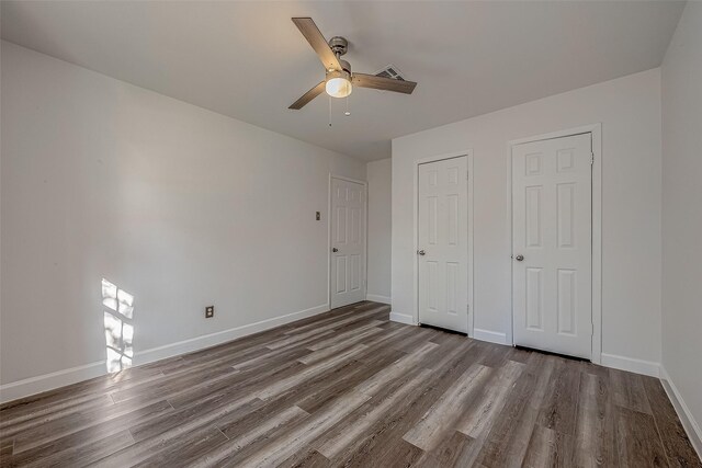 unfurnished bedroom with ceiling fan, wood-type flooring, and two closets