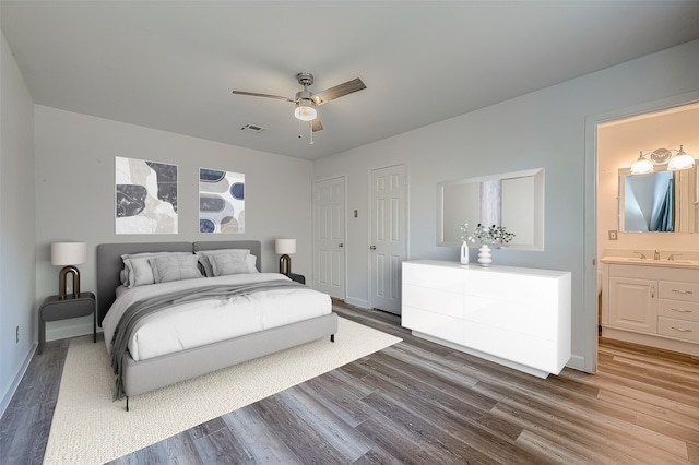 bedroom with ensuite bathroom, two closets, ceiling fan, sink, and hardwood / wood-style floors