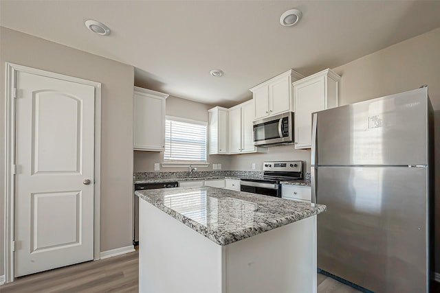 kitchen with light stone countertops, appliances with stainless steel finishes, light wood-type flooring, a center island, and white cabinets