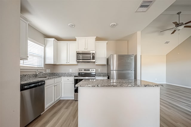 kitchen with appliances with stainless steel finishes, white cabinets, a center island, and light wood-type flooring