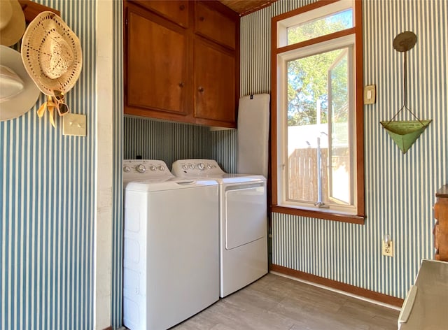 clothes washing area with cabinets, washing machine and clothes dryer, and light hardwood / wood-style floors