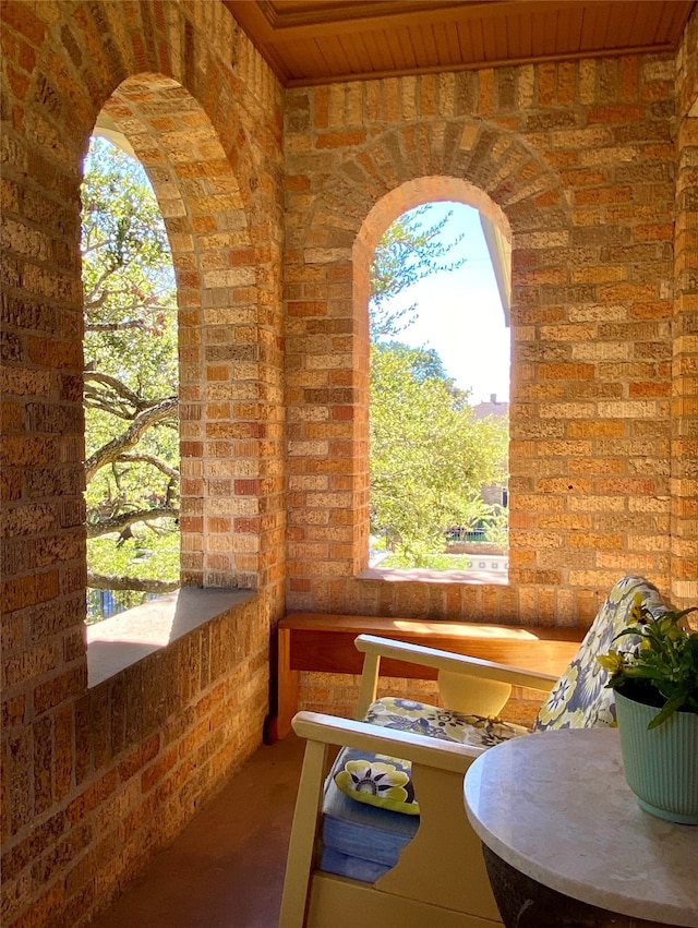 exterior space featuring wood ceiling, brick wall, plenty of natural light, and concrete flooring