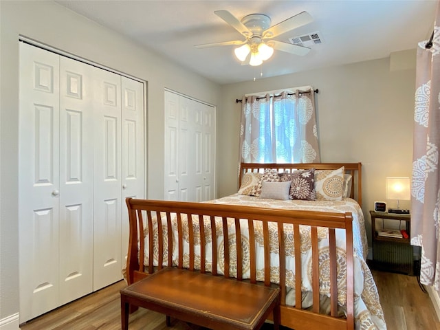 bedroom with multiple closets, hardwood / wood-style floors, and ceiling fan