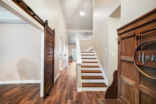 staircase with hardwood / wood-style floors, a barn door, and high vaulted ceiling