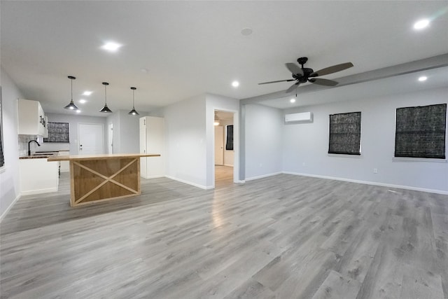 unfurnished living room featuring a wall unit AC, light hardwood / wood-style floors, sink, and ceiling fan