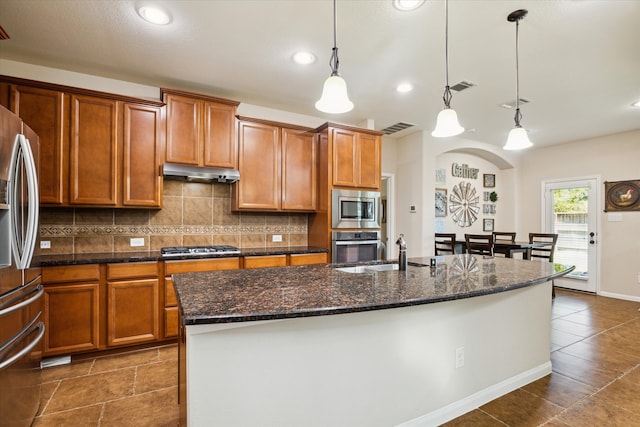 kitchen with decorative light fixtures, an island with sink, sink, backsplash, and stainless steel appliances