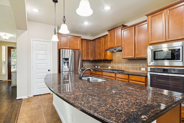 kitchen featuring sink, a kitchen island with sink, backsplash, hanging light fixtures, and stainless steel appliances