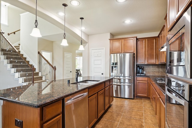 kitchen featuring pendant lighting, sink, backsplash, stainless steel appliances, and a center island with sink