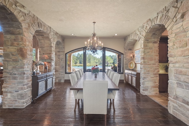 unfurnished dining area with decorative columns, a textured ceiling, dark hardwood / wood-style floors, and a chandelier