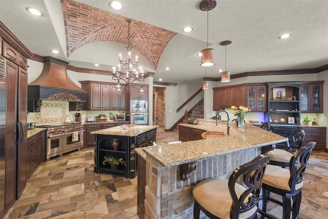 kitchen featuring kitchen peninsula, a spacious island, built in appliances, sink, and decorative light fixtures