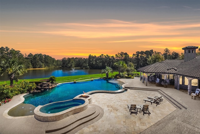 pool at dusk featuring a patio, an in ground hot tub, and a water view