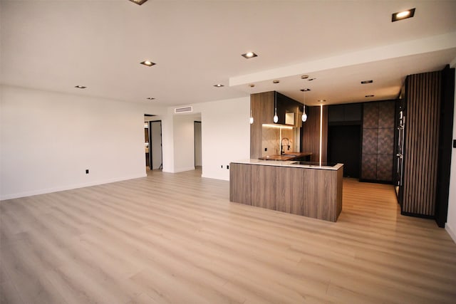 kitchen featuring sink, light hardwood / wood-style flooring, kitchen peninsula, and decorative light fixtures