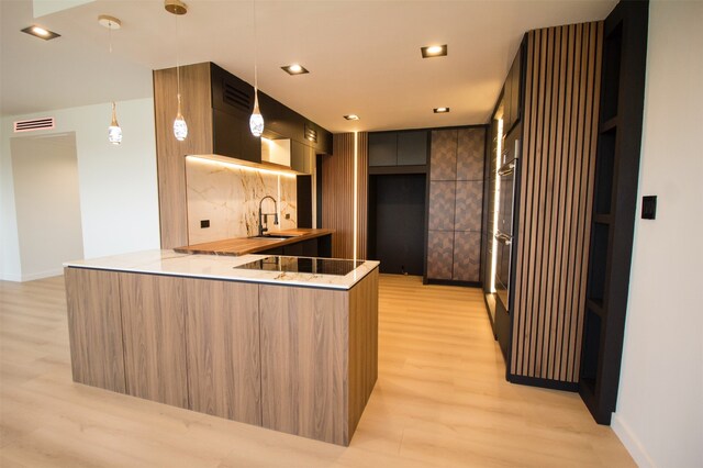 kitchen featuring black electric stovetop, light hardwood / wood-style flooring, kitchen peninsula, backsplash, and sink