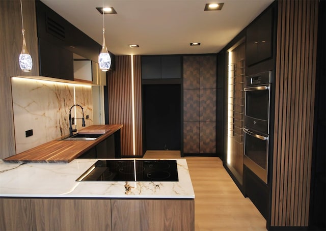 kitchen featuring black electric stovetop, sink, double oven, pendant lighting, and light hardwood / wood-style flooring