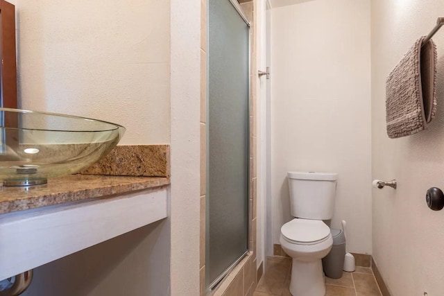 bathroom featuring a shower with shower door, tile patterned floors, and toilet