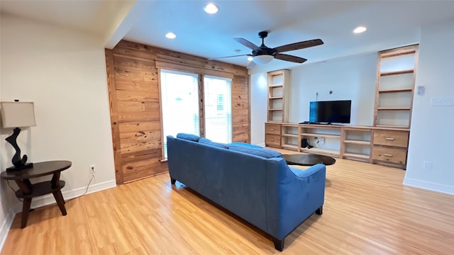 living room with ceiling fan, wood walls, built in features, and light wood-type flooring