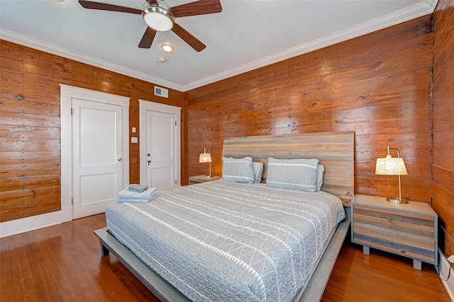 bedroom featuring hardwood / wood-style flooring, crown molding, ceiling fan, and wood walls