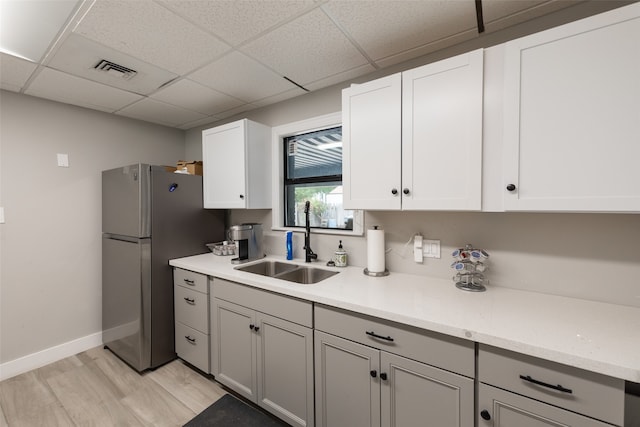 kitchen with light hardwood / wood-style flooring, stainless steel fridge, sink, white cabinetry, and a paneled ceiling