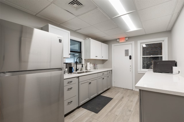 kitchen featuring stainless steel refrigerator, light hardwood / wood-style flooring, gray cabinetry, a drop ceiling, and sink