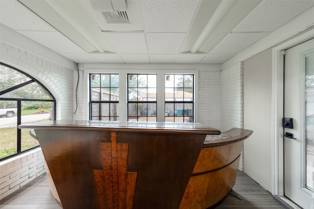 bar with a paneled ceiling, a healthy amount of sunlight, wood-type flooring, and brick wall