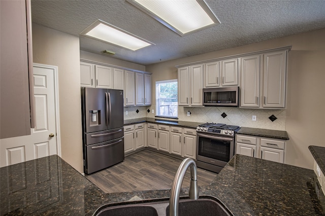 kitchen with sink, backsplash, dark hardwood / wood-style flooring, stainless steel appliances, and dark stone counters