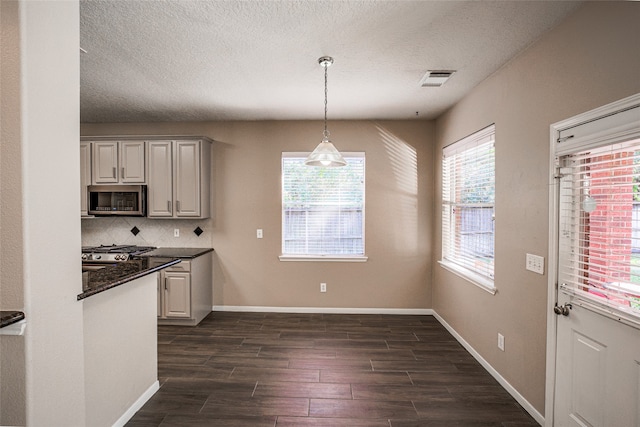 kitchen with hanging light fixtures, backsplash, appliances with stainless steel finishes, a textured ceiling, and dark wood-type flooring